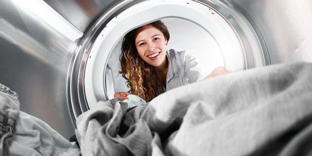 A smiling woman removes dry clothes from a clothes dryer